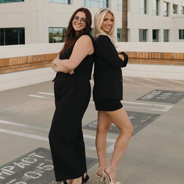 Angi and Riley standing back-to-back in black outfits outdoors.