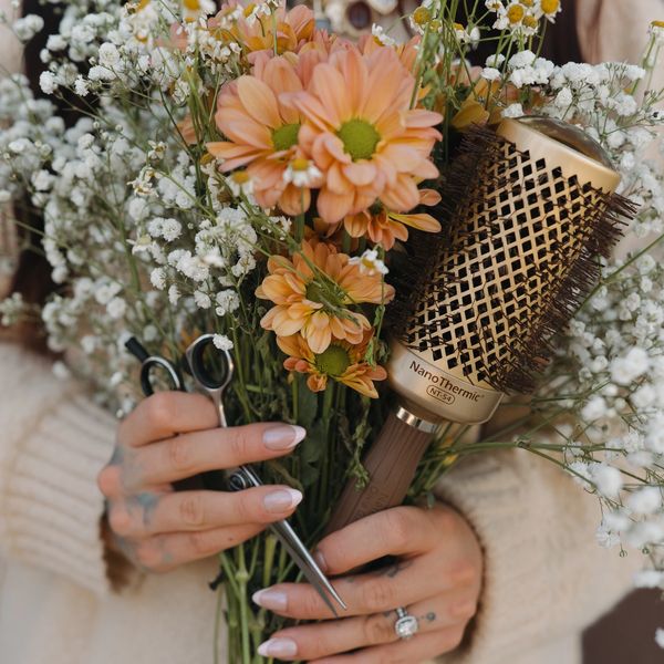 Close-up of hands holding flowers with hair scissors, symbolizing salon services.