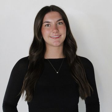 Smiling team member with long dark hair in black top, white arch.