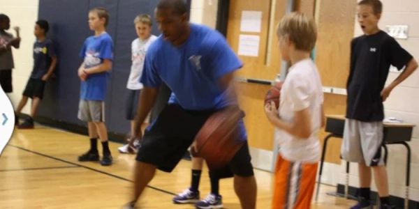 Coach training kids in basketball drills inside a gym.