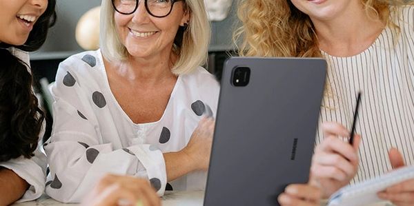 Three women happily collaborating with a tablet and notebook.