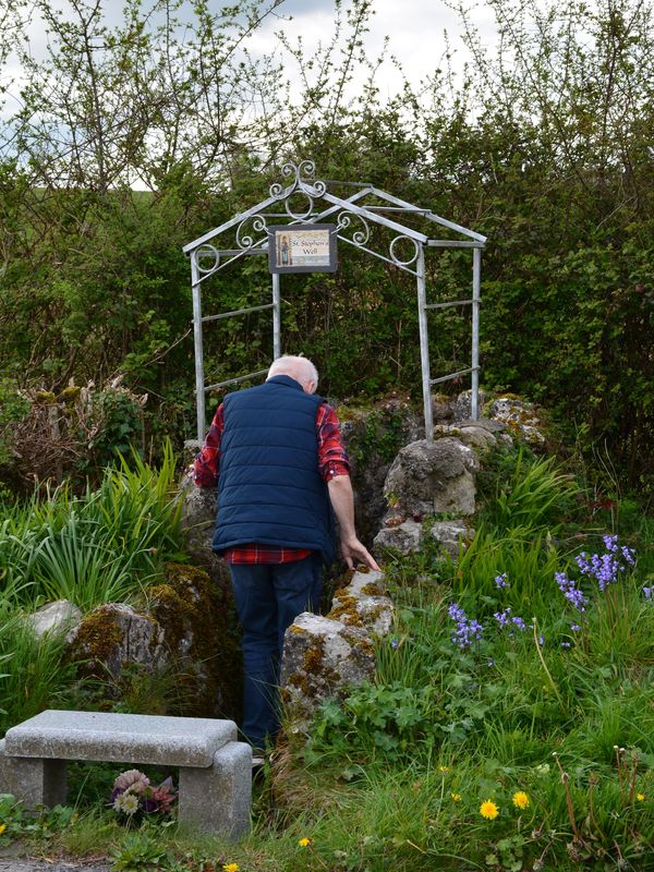 Man standing at a stone well surrounded by greenery.