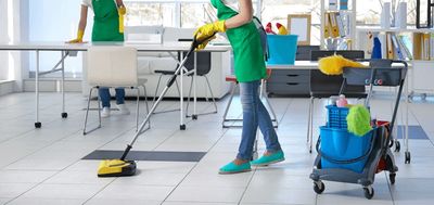 Two people cleaning a bright, modern office space with mops and cleaning supplies.