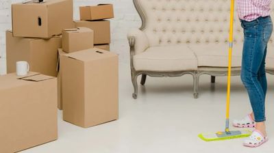 Child standing near packed moving boxes and sofa with a mop.