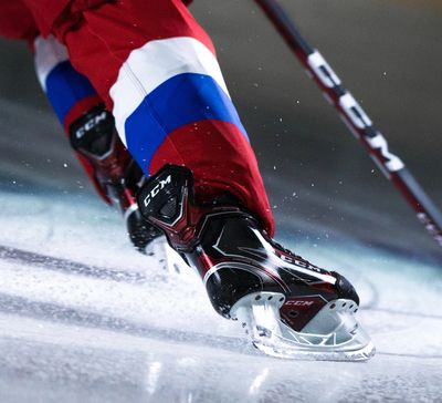 A player's lower legs and CCM brand skates, skating on ice. A CCM brand hockey stick is visible, and