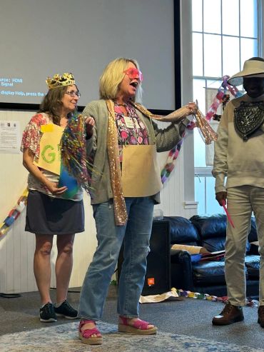 Three adults wearing playful costumes inside a room with paper decorations.
