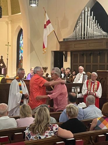 Two men embrace in a church during a ceremony with clergy present.