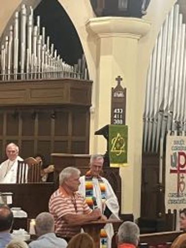 Man speaking at church pulpit with clergy present.