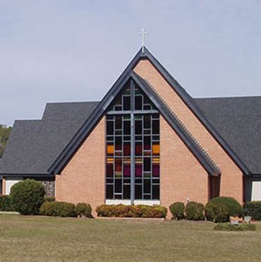Brick church with stained glass window and cross on top.