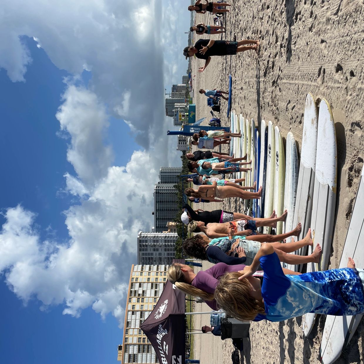Surf lesson on a sunny beach with kids lined up on surfboards.