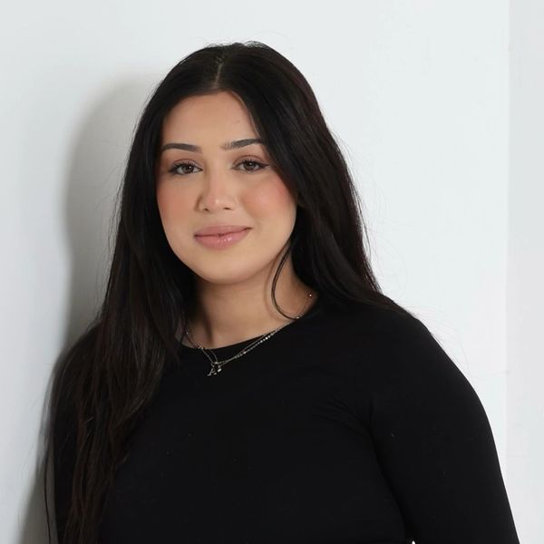 A woman with long dark hair wearing a black top smiles gently at the camera.