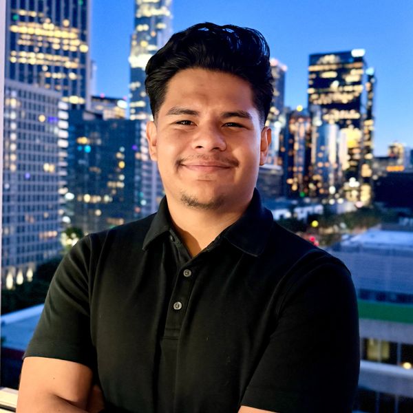 Smiling man in black polo shirt with city skyline at dusk.