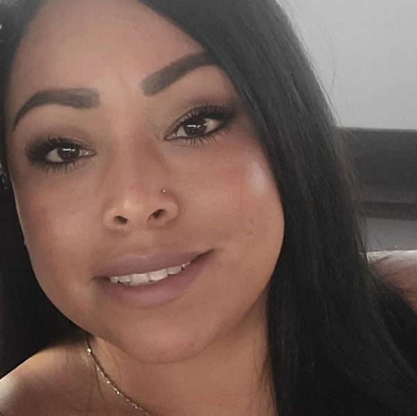 Close-up portrait of a smiling woman with long black hair and a nose piercing.