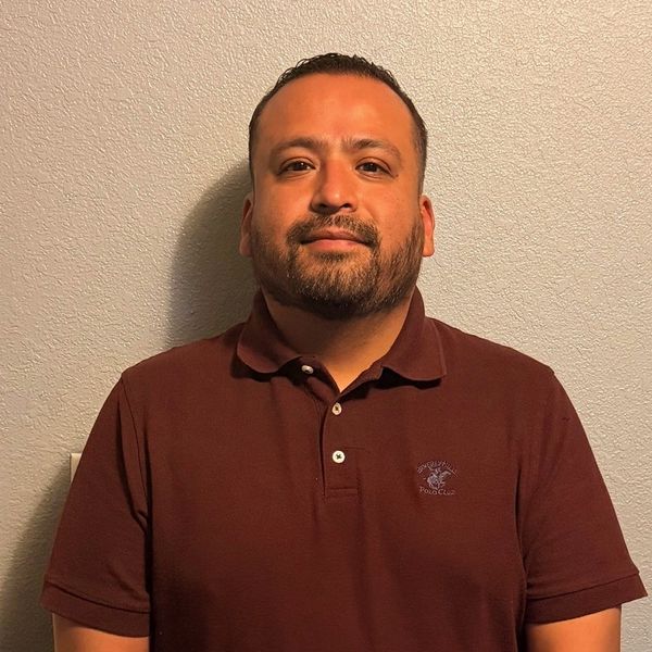 Man in a maroon polo shirt standing against a textured wall.