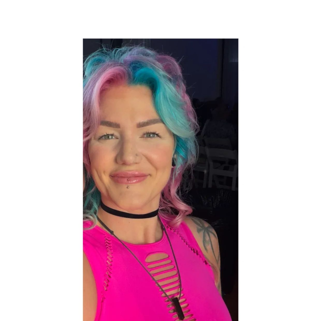 Woman with colorful hair and bright pink top smiling.