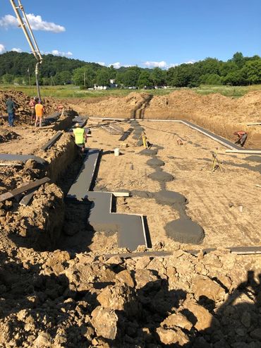 Workers pouring concrete foundation at a construction site on a sunny day.