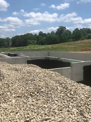 Concrete foundation with gravel pile under a partly cloudy sky in a rural area.