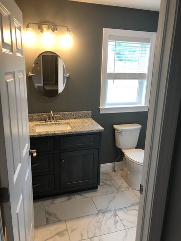 Modern bathroom with dark vanity, granite countertop, and marble tile floor.