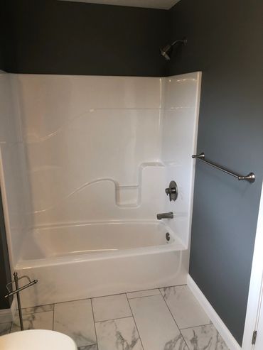 Clean white bathtub with gray walls and marble floor tiles.