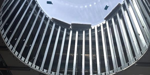 Looking up at a circular glass ceiling with metal beams.