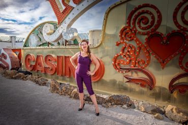 Woman in purple jumpsuit posing in front of a vintage casino sign outdoors.
