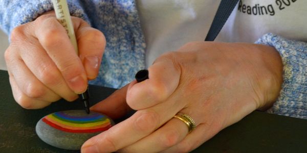 Clsoe-up of a woman's hands drawing a rainbow on a rock