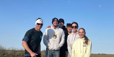 Group of six people smiling outdoors under a clear blue sky.
