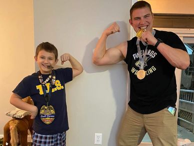 Two people flex muscles and show off medals indoors.