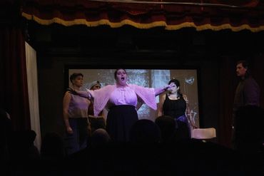A theatrical performance with four actors on stage, one passionately singing or speaking.