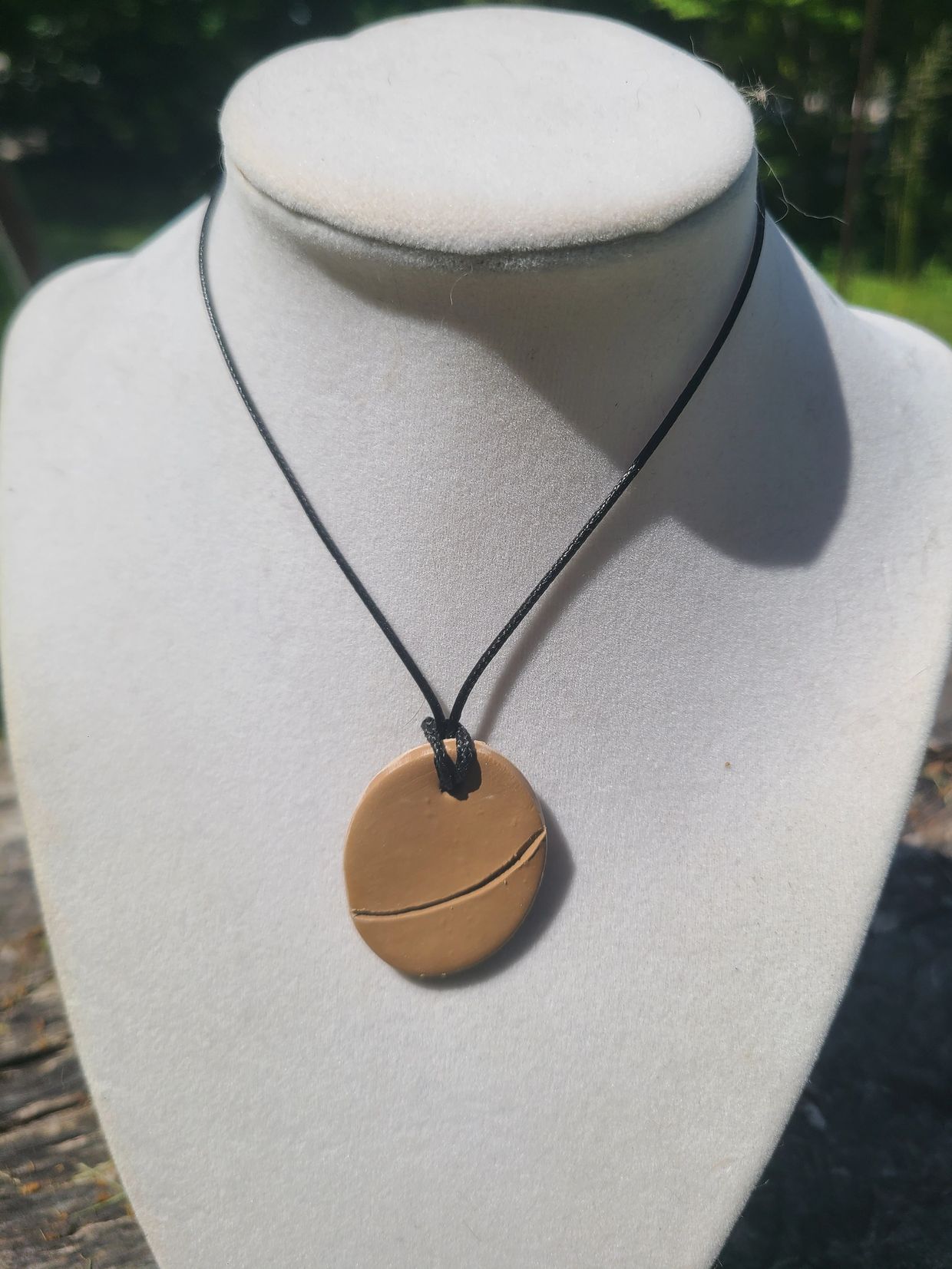Minimalist round tan pendant on a black cord displayed on a white bust.