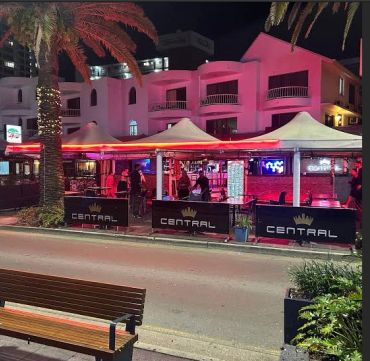 Outdoor night scene of a lit Central branded cafe with tents and palm trees.
