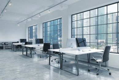 Interior office space with desks and chairs and three windows.