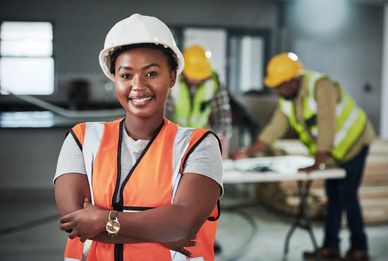 Construction worker smiling in the foreground as two colleagues in the background review blueprints.