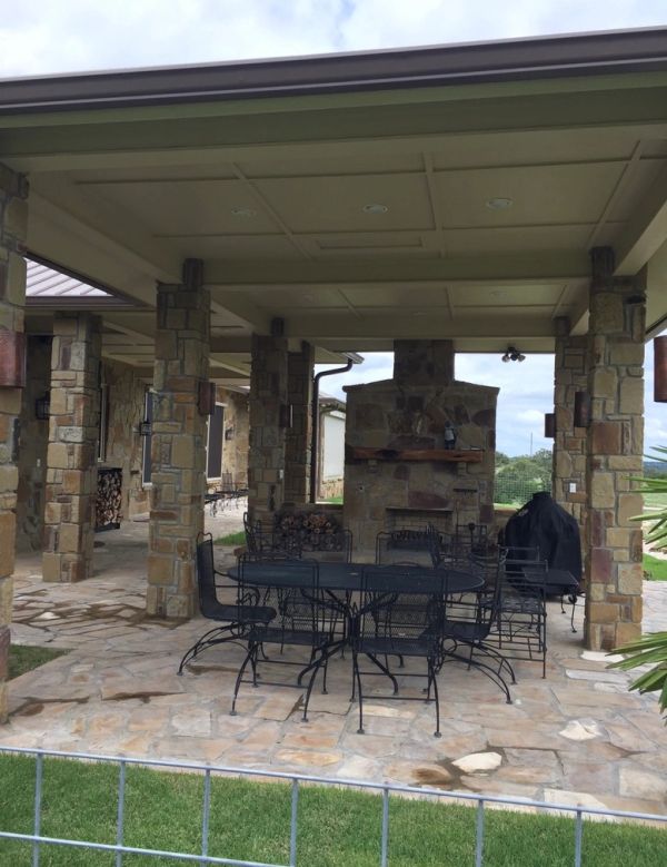 Covered outdoor patio with stone pillars and metal furniture around a fireplace.