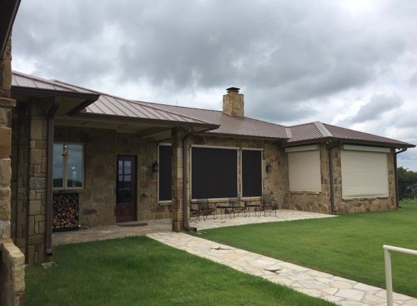 Stone house with metal roof and closed shutters on windows under cloudy sky.