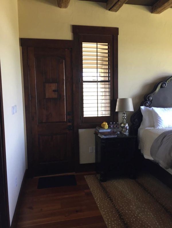 Cozy bedroom corner with a wooden door, shuttered window, and bedside table.