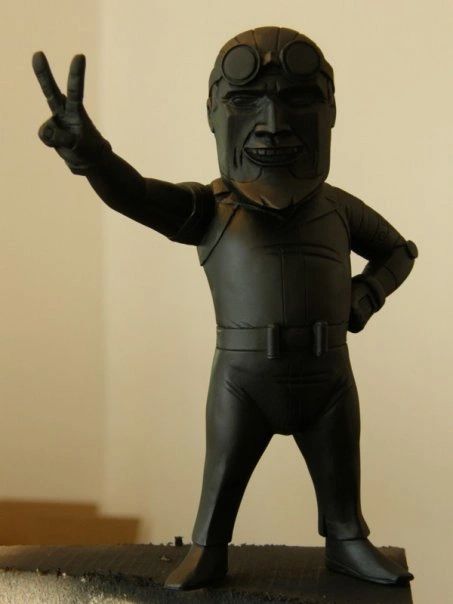 A black statue of a man giving a peace sign with goggles on.