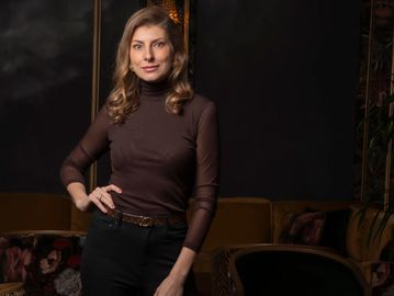Femme posant avec confiance dans un pull marron et pantalon noir.