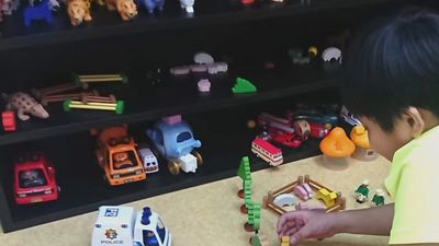 A child playing with toy vehicles and figures on a table.