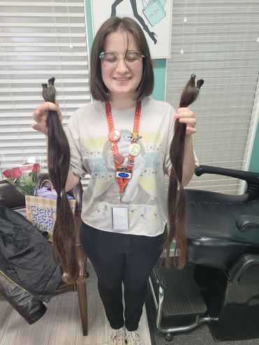 A smiling person holding two long cut hair sections indoors.