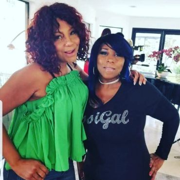 Two women posing indoors, one in green and the other in black.