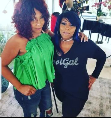 Two women posing indoors, one in green and the other in black.