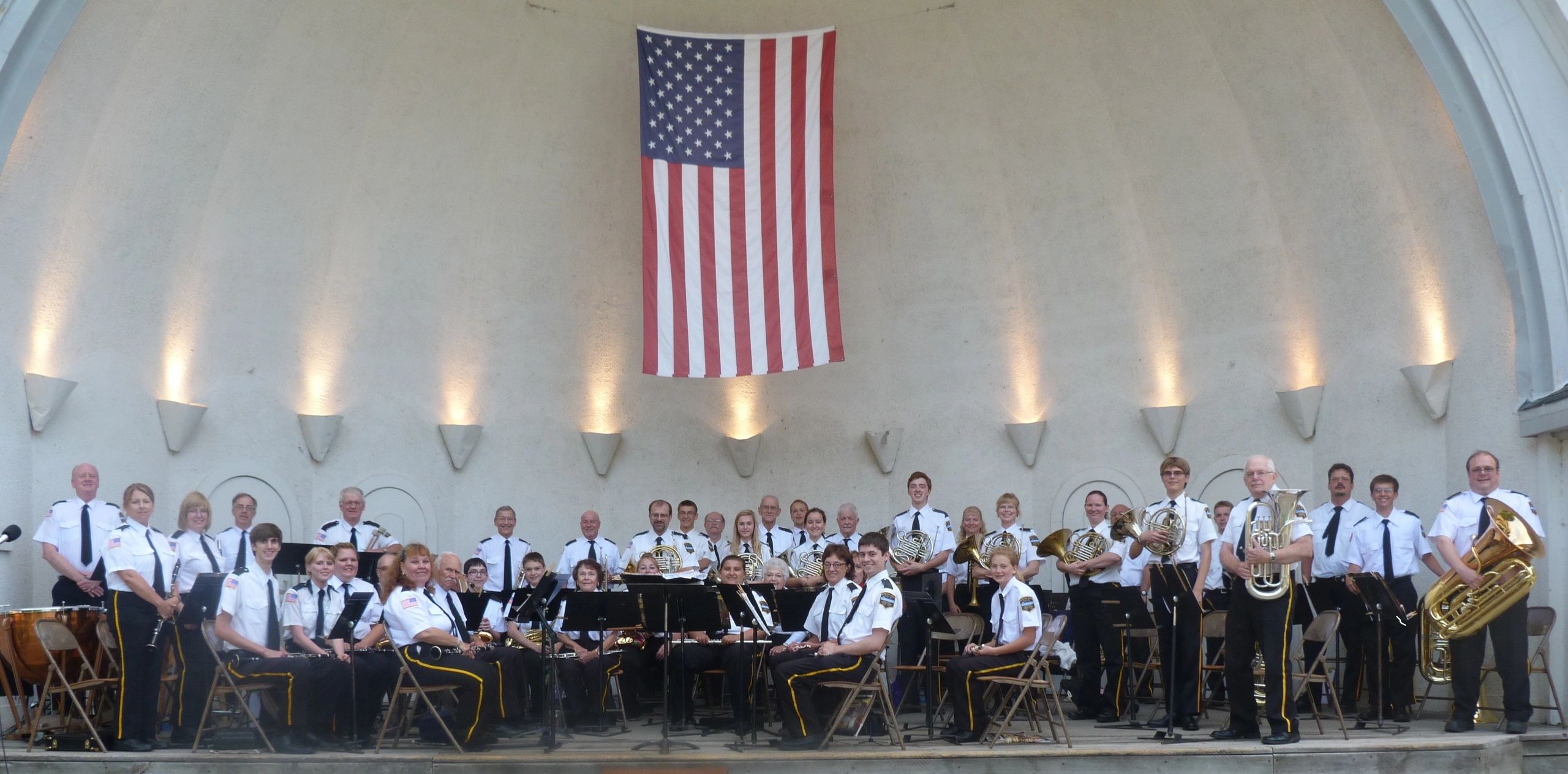 Large band in uniform posing with American flag on stage.