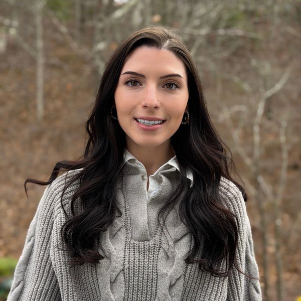 Woman with long dark hair wearing a gray knitted sweater outdoors.