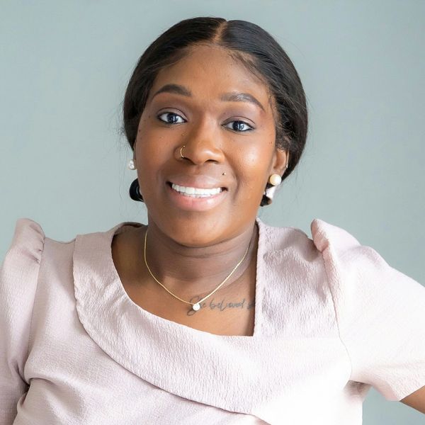 Smiling woman with pearl earrings and a light pink top.