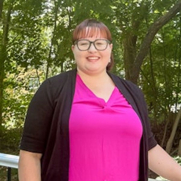 Smiling woman in a bright pink top and black cardigan outdoors.