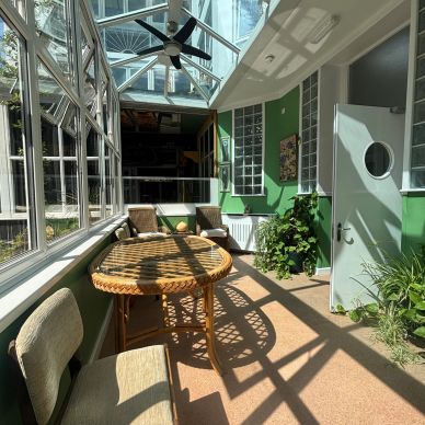 Bright sunlit sunroom with wicker furniture and green walls.