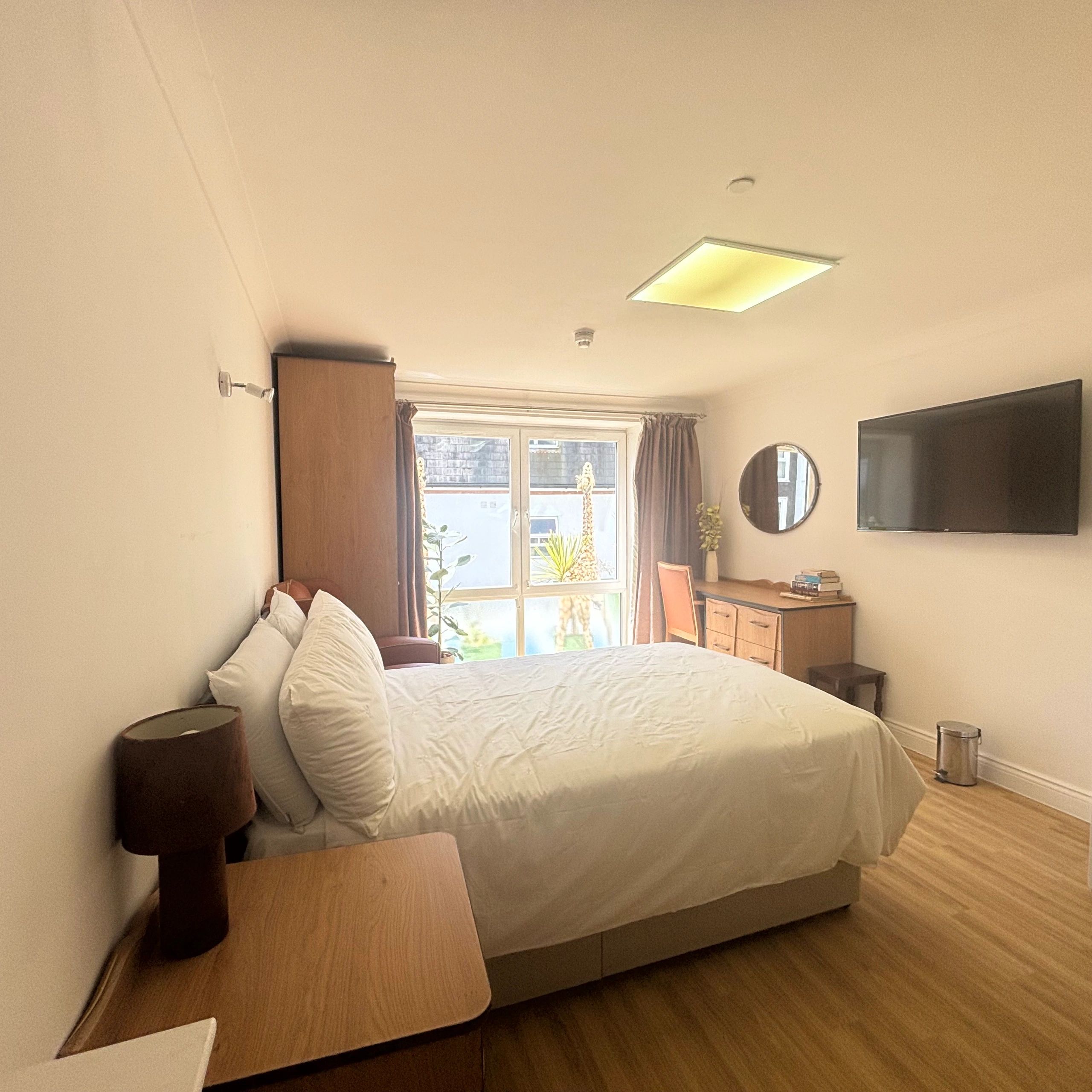 Cozy bedroom with natural light, wooden furniture, and a wall-mounted TV.