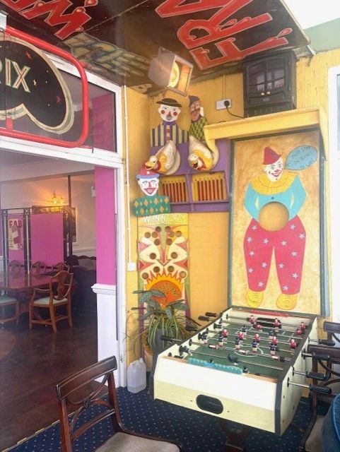 A colorful vintage arcade corner with clown decorations and a foosball table.