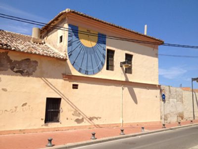 Sundial painted on the side of a beige building under a clear blue sky.